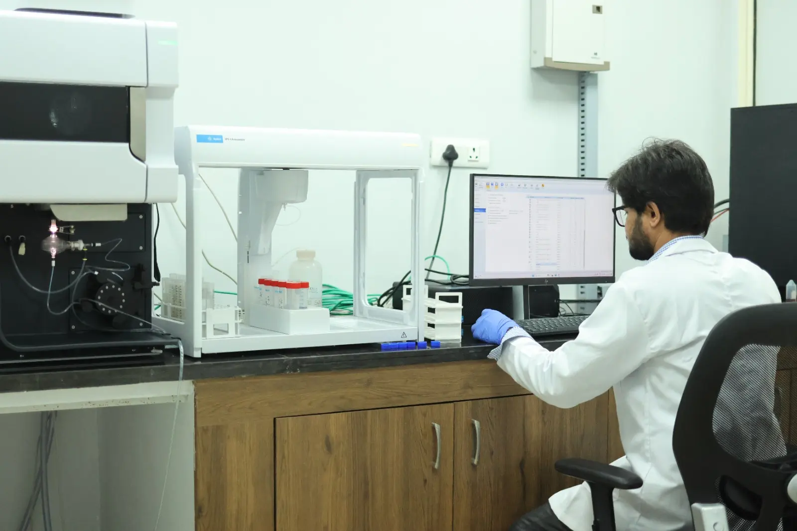 A technician at a computer beside an analyser with an automatic sampler