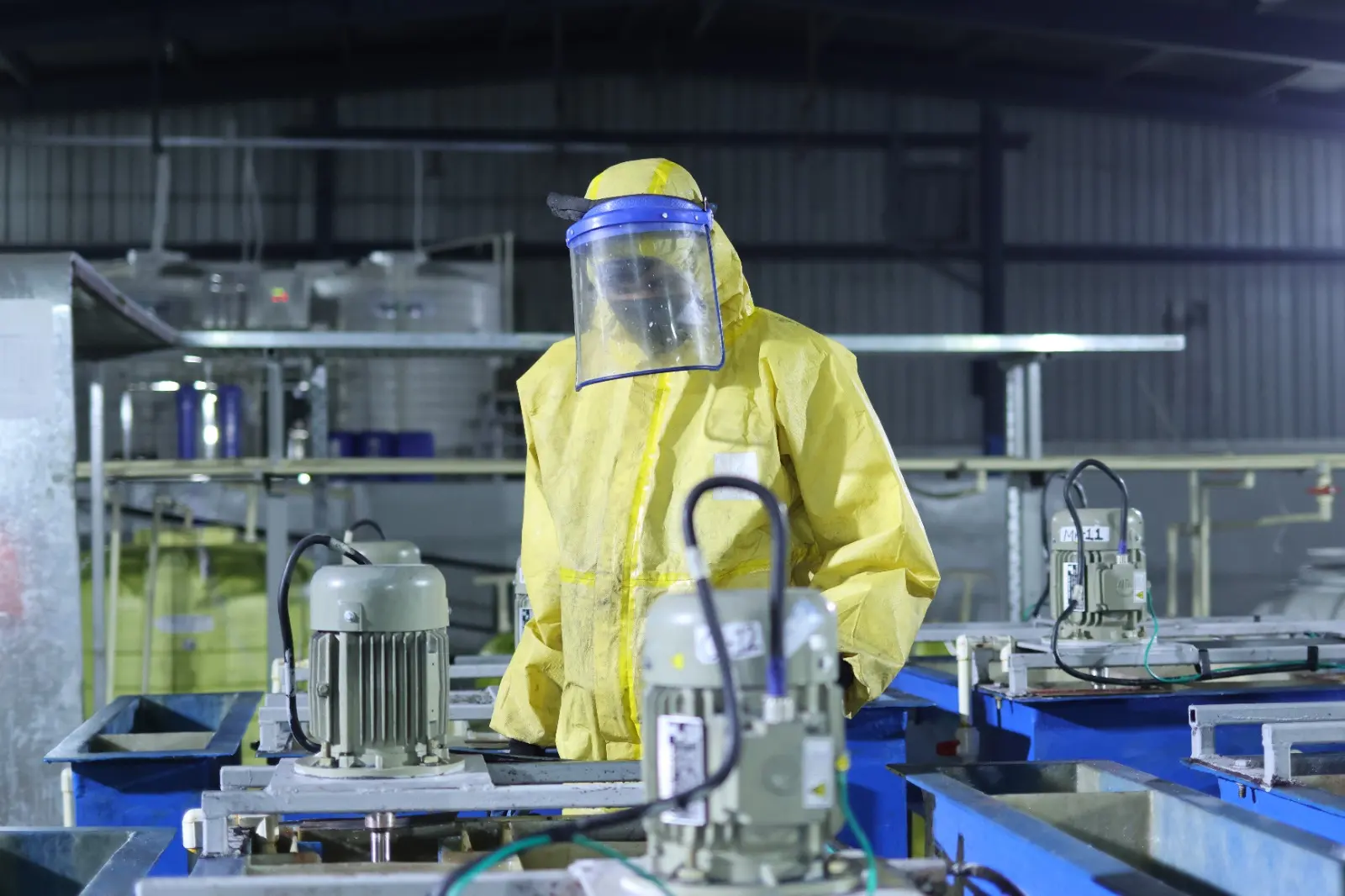 A worker in a yellow protective suit and face shield beside a motor on the processing line